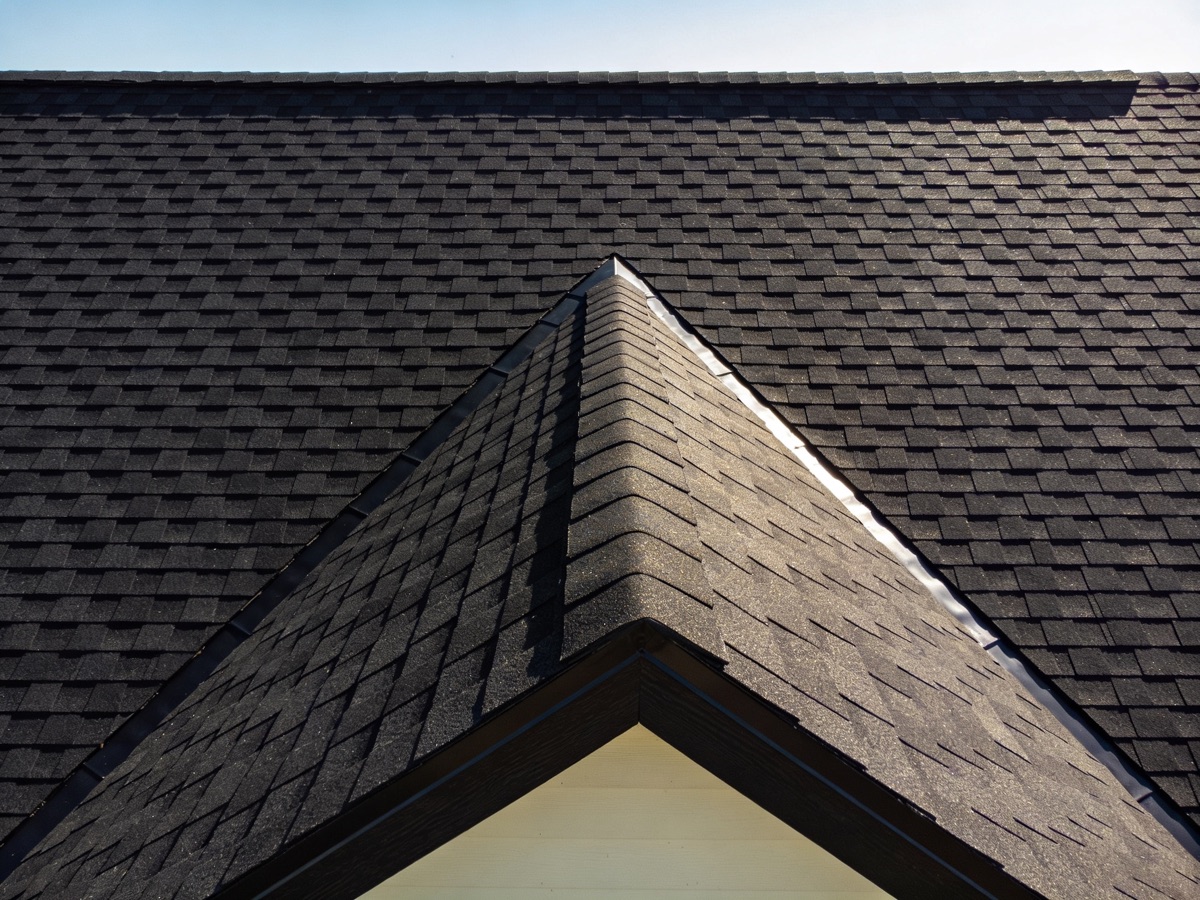 Drone aerial close-up of a freshly completed black asphalt-shingle roof with a sharp gable peak