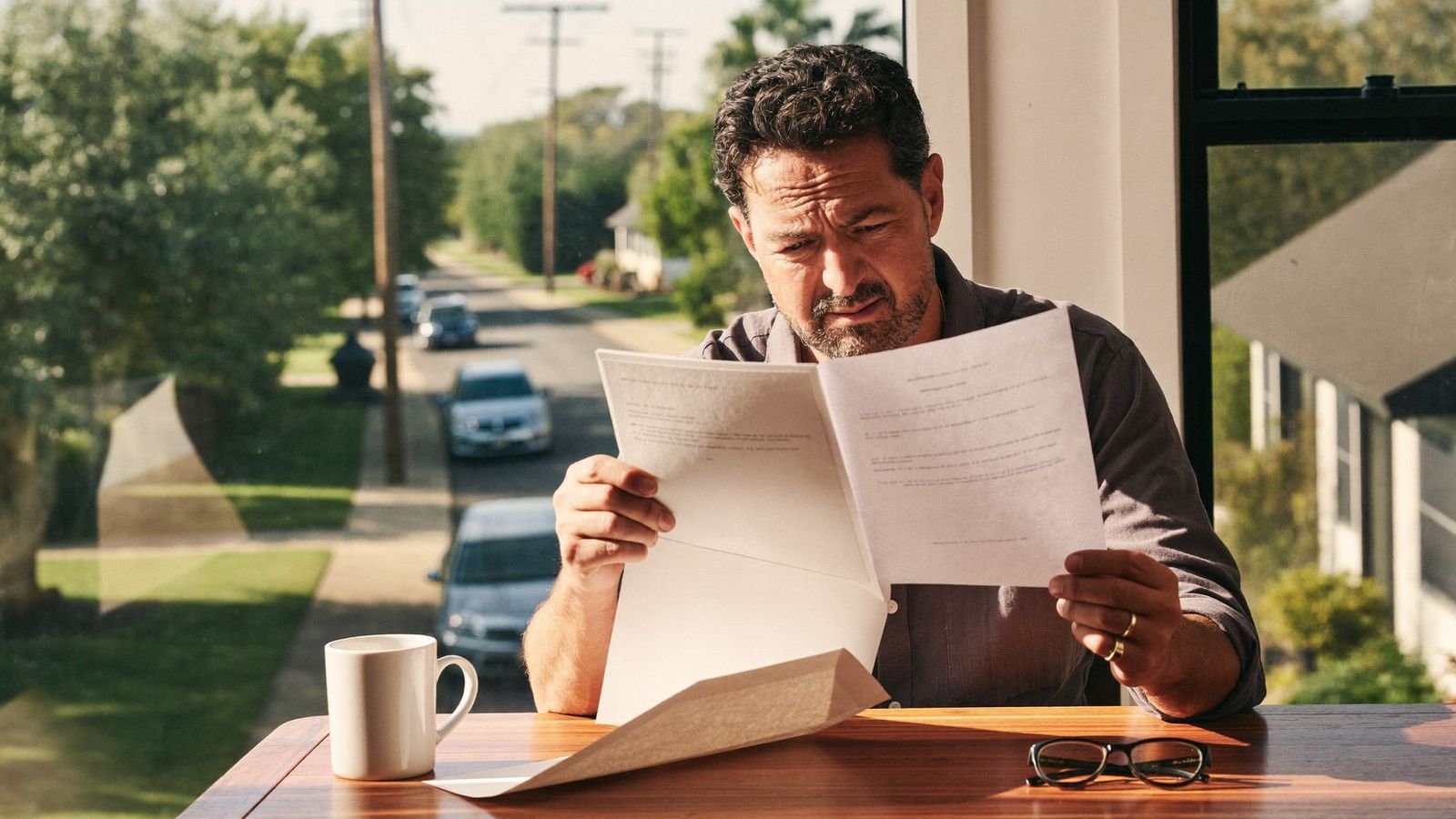 Homeowner at a kitchen table reading a roof non-renewal letter from their insurance company