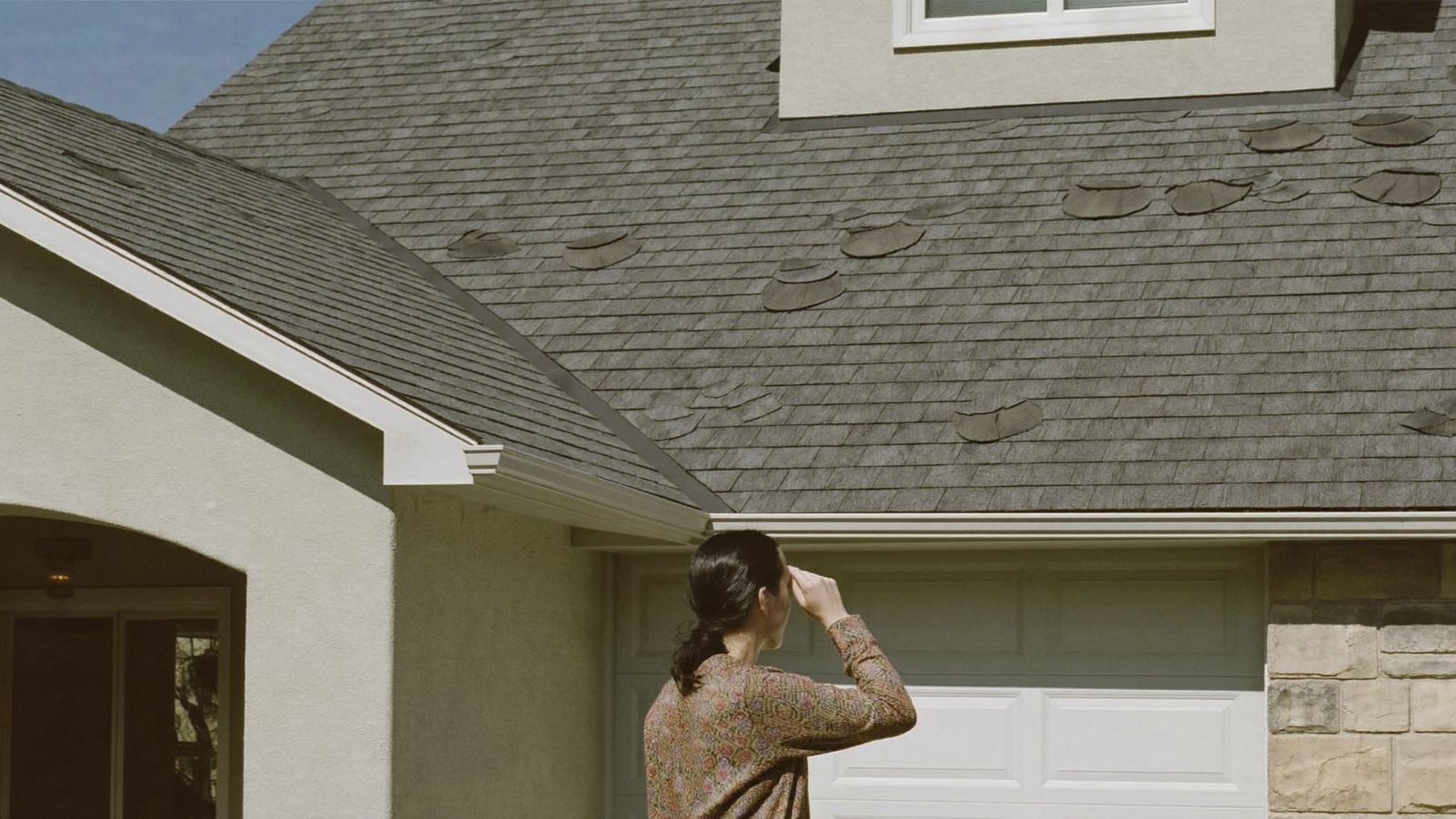 Homeowner looking up at worn, curling shingles on a Houston home